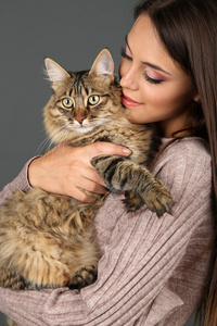 美丽的年轻女子控股猫在灰色的背景上