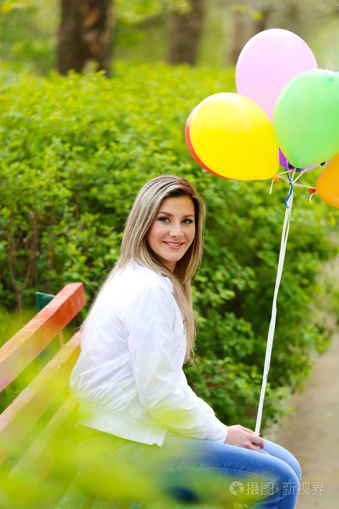幸福着五颜六色的气球在公园的长椅上坐着的女人
