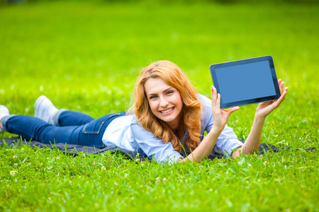 金发女人躺在绿色的草在手里的平板电脑