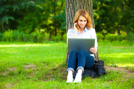 美丽的女人坐在公园的笔记本电脑
