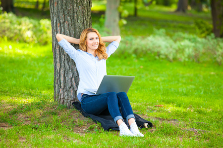 美丽的女人坐在公园的笔记本电脑