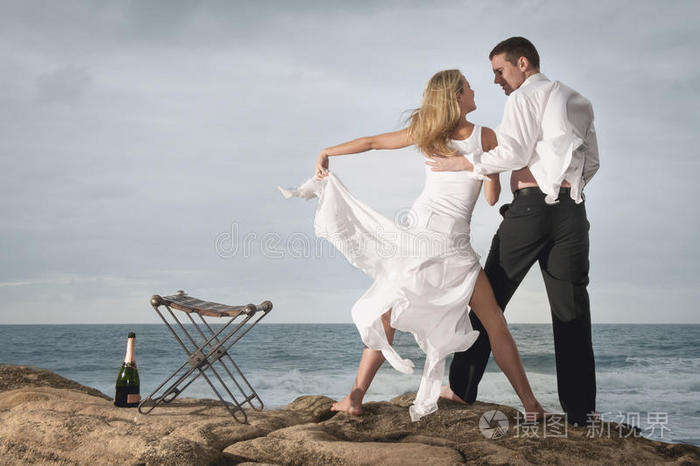 年轻浪漫的情侣在海滩岩石上跳舞香槟