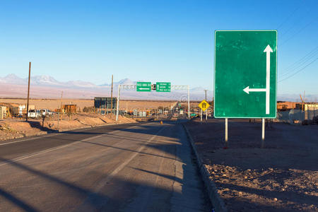 在阿塔卡马沙漠中，一个绿色路标立在一条公路旁，一个箭头朝上，一个向右