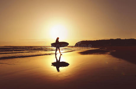 日出时冲浪者沿着海滩散步的剪影