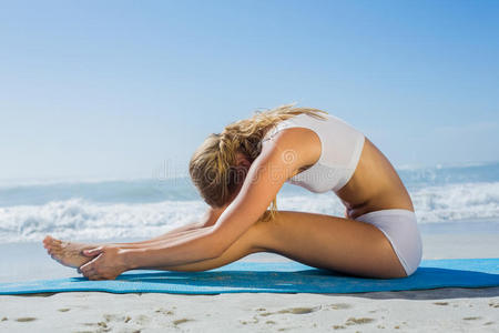 美丽的金发美女坐在海滩前弯姿势