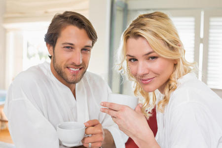 穿着浴袍的可爱情侣在一起喝咖啡，对着镜头微笑