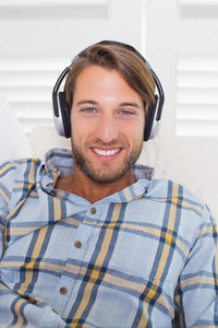 随意微笑的男人躺在沙发上听音乐