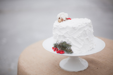 与杉木和红色浆果的一枝的白色婚礼蛋糕。