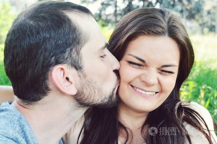 男人的脸颊上亲吻女人虽然她是笑着并做鬼脸