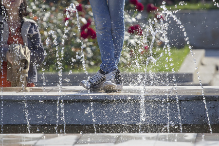 水滴从喷泉与年轻女孩的脚，穿着牛仔裤