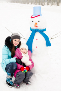 带着笑容的小女孩雪人的年轻女子在冬季的一天
