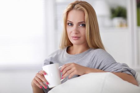 年轻漂亮的女人和在家里的沙发上喝杯