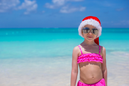可爱的小女孩在热带海滩上的红色圣诞帽