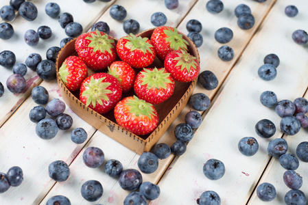 新鲜的草莓和蓝莓在组件上的心形状篮子里