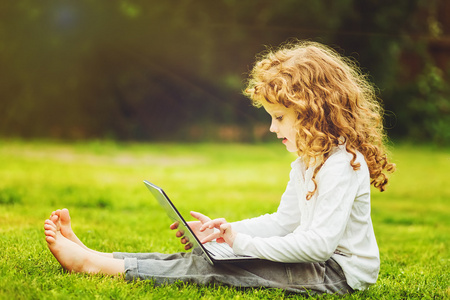 快乐的惊讶的孩子,坐在草地上的笔记本电脑照片