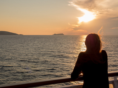 女孩从邮轮的甲板上看着海上的日落照片