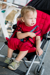 蹒跚学步的男孩坐在红色的婴儿小推车