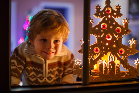微笑的男孩在圣诞节的时候和控股可以站在窗口