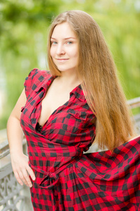 有一头棕色的长发，在大自然中一个美丽的年轻女子的画像。女孩穿着格子呢外衣的阳台上摆姿势