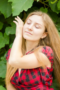 有着一头棕色的长发女孩靠在墙上的绿色的树叶构成美丽的年轻女子的画像