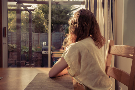 手指窗外年轻女子坐在餐桌旁,看着窗外照片