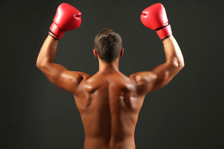 英俊年轻肌肉型男用拳击手套在深色背景上