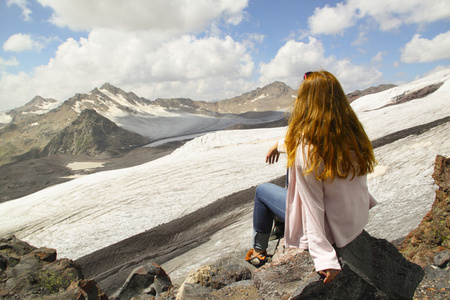 年轻的女孩坐在悬崖的边缘，看着天空