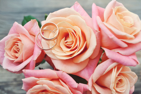在粉红色的玫瑰花的美丽婚礼花束上的两个金色的订婚戒指。