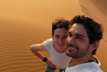 一对年轻夫妇在攀登到顶部的红色沙丘之海的摩洛哥 erg 巨大的沙丘时自拍照
