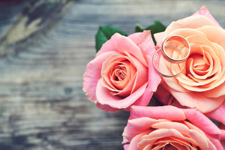 在粉红色的玫瑰花的美丽婚礼花束上的两个金色的订婚戒指。