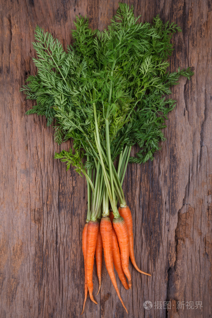 束新鲜胡萝卜与绿色叶子在木制的背景照片-正版商用图片1glmdq-摄图新