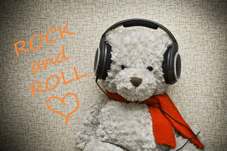 泰迪熊与橙色的围巾在耳机上听音乐。摇滚乐的爱人