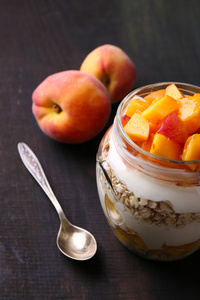 健康酸奶鲜桃和牛奶什锦早餐在玻璃罐中，木制的背景上