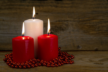 三个燃烧的圣诞蜡烛，旧的木制表面上