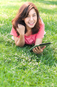 使用 tablet 室外躺在草地上的年轻女子微笑