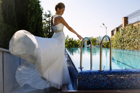 美丽的新娘在典雅婚纱礼服在游泳池边摆姿势