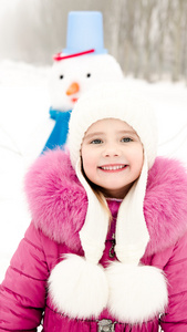 微笑的小女孩，用雪人在冬季的一天的肖像