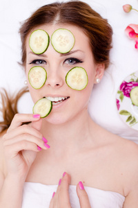 绿色天然矿泉治疗 开心的美丽金发碧眼的年轻女子将黄瓜片应用于她脸上的皮肤开心的笑  看着照相机上白色背景特写肖像图像