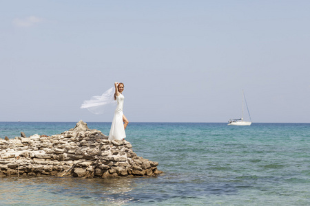 美丽的新娘站在悬崖上迷人的白色婚纱在海面之上