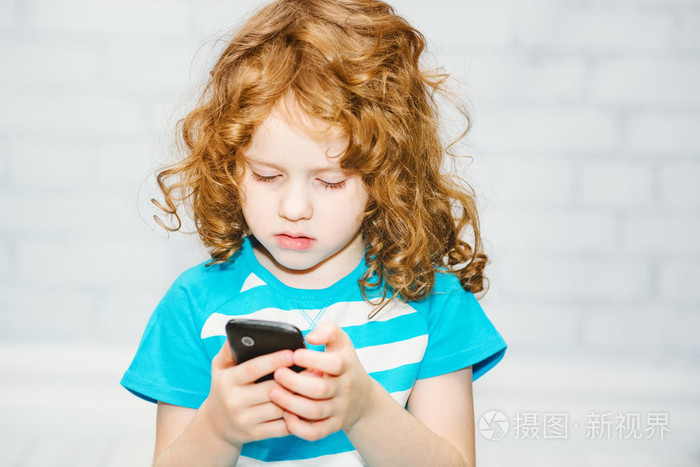 在明亮的背景上的智能手机上玩的小女孩