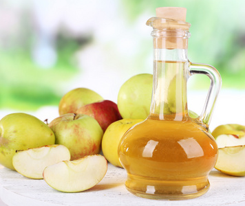 苹果醋玻璃瓶和成熟的新鲜苹果，木制的桌子，对自然背景上