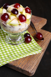 健康酸奶与新鲜的葡萄和苹果片和牛奶什锦早餐在玻璃碗里，木制的背景上