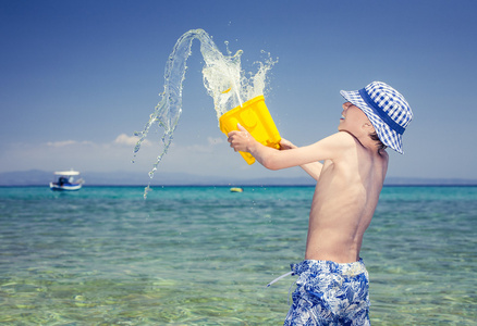 巴拿马在海里扔水笑一黄色玩具桶玩有趣的小男孩