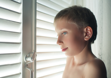 一个带有百叶窗带着滑稽的表情的窗口前摆姿势的小男孩