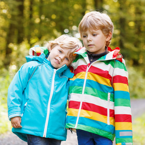 两个小兄妹男孩在五颜六色的雨衣和靴子走路