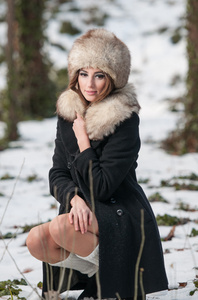 画像的年轻漂亮的女人，户外拍摄冬天的景色。感性的黑发女孩摆在一个公园里的外套和毛皮帽覆盖着雪。时尚女性在一个寒冷的日子