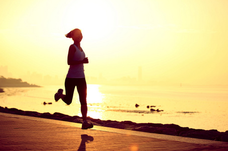 运行在海边的跑步运动员。女人健身剪影日出慢跑锻炼健康概念