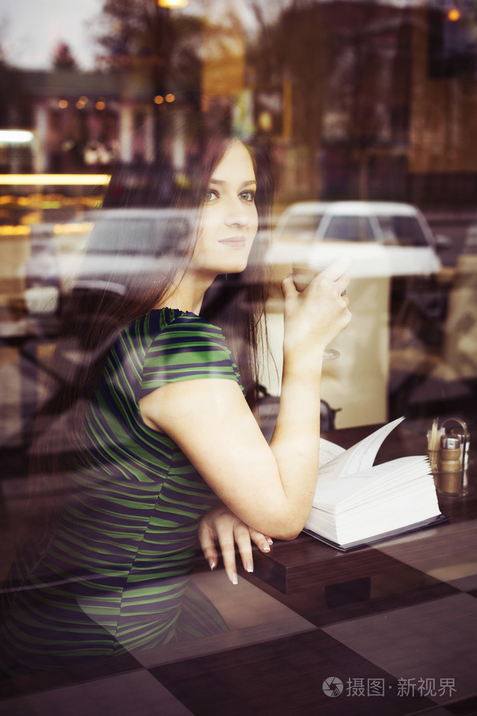 黑发女人坐在咖啡馆里读书,学习和喝咖啡