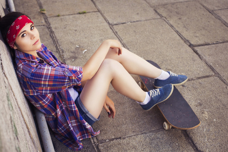 布鲁内特十几岁的女孩在行家装备 牛仔短裤，keds，格子衬衫，帽子 与滑板在公园户外活动。副本空间