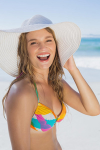 海滩上穿着比基尼，戴着草帽的漂亮女孩对着镜头微笑